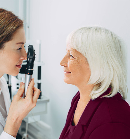 A female optometrist examines an older female patients eyes. Eye exams are essential to preventing common eye diseases as you age.