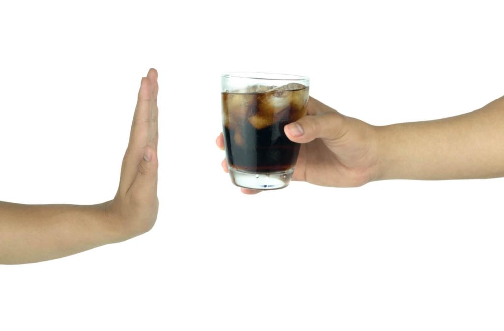 A hand refusing to drink soda, limiting your caffeine intake to avoid twitching eyes.