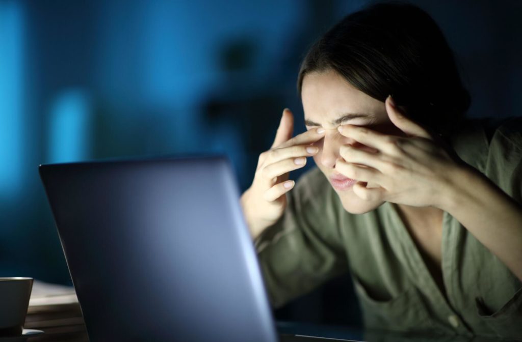 A woman in front of her computer is touching her eyelids with her both index fingers to massage her eyes with eyestrain after long hours on the screen.