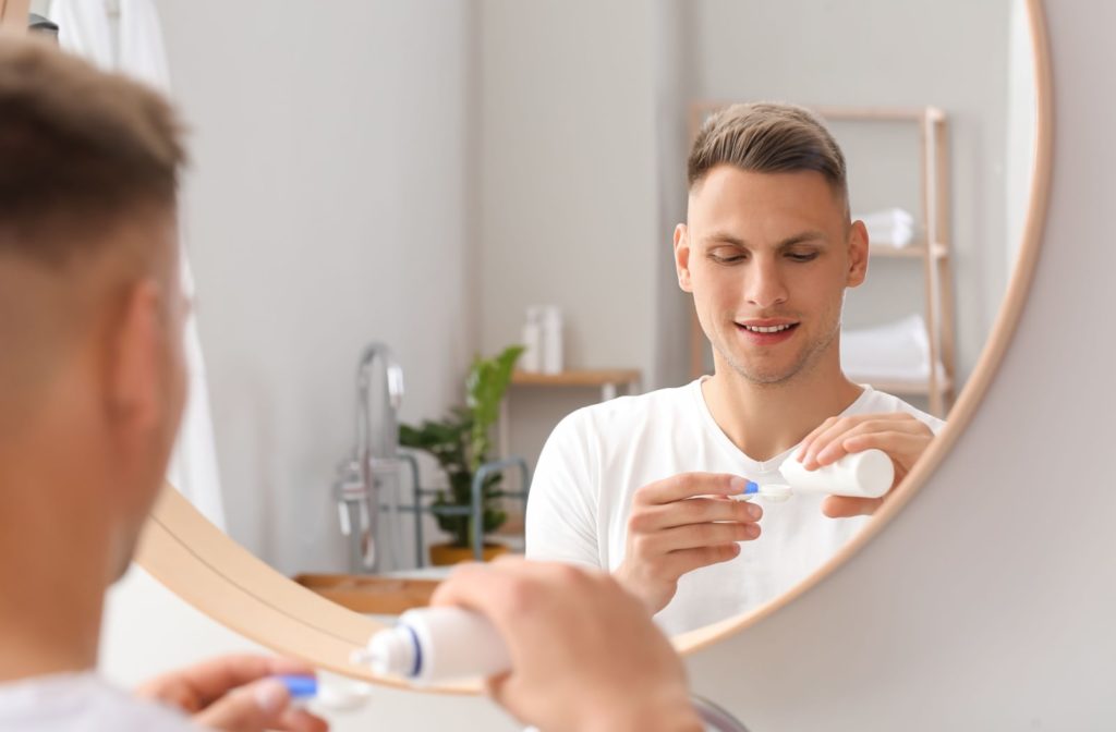 A young man in front of a mirror putting a contact lens solution to a case of contact lenses.