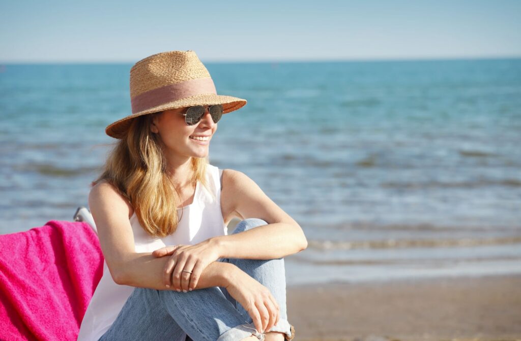 A woman sits on a chair on a beach while she is wearing polarized sunglasses.